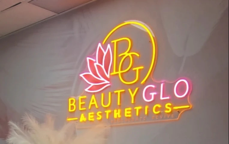 The BeautyGlo lotus and halo logo lit in neon on the blush feather wall at reception