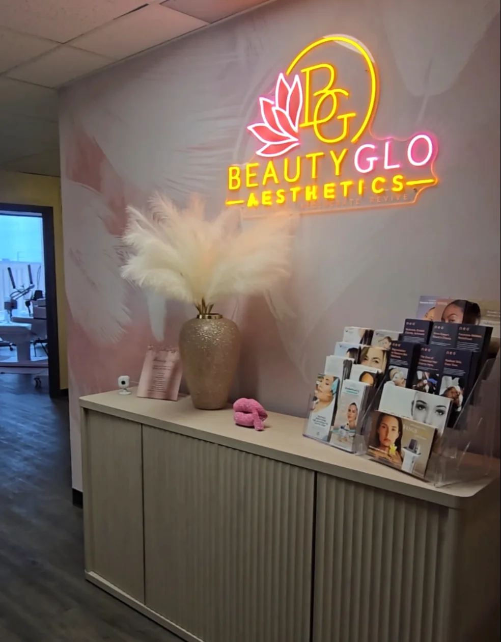 BeautyGlo reception: the lotus and halo logo lit in neon on a blush feather wall, above a fluted cabinet